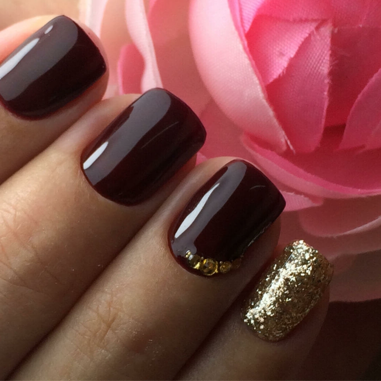 Decorazioni unghie di colore bordeaux con piccoli brillantini sul dito anulare e glitter sul mignolo 